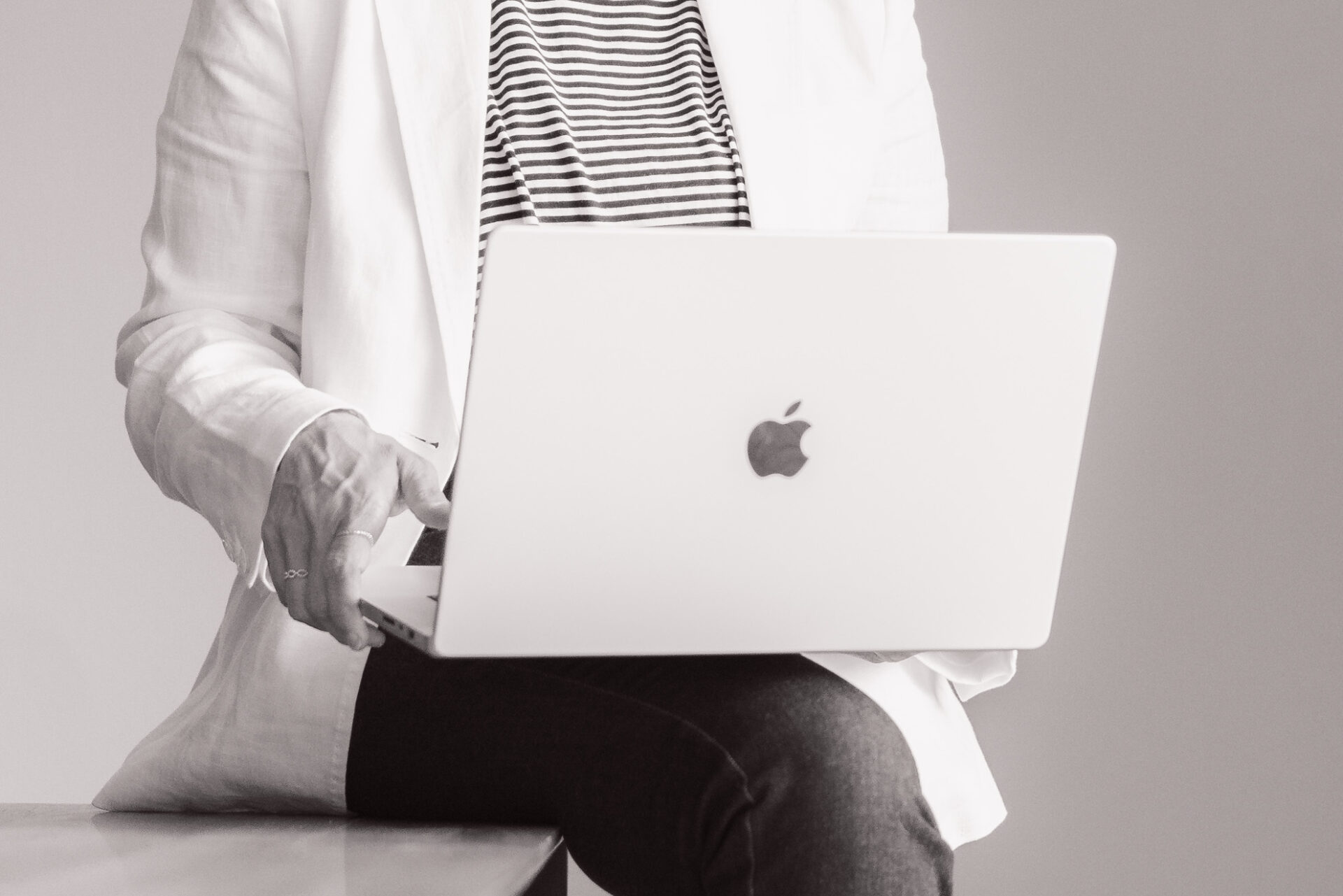 Janine Wettstein, Bildausschnitt von mit dem Gesäss auf der Tischkante sitzend, den Laptop auf den Knien haltend.